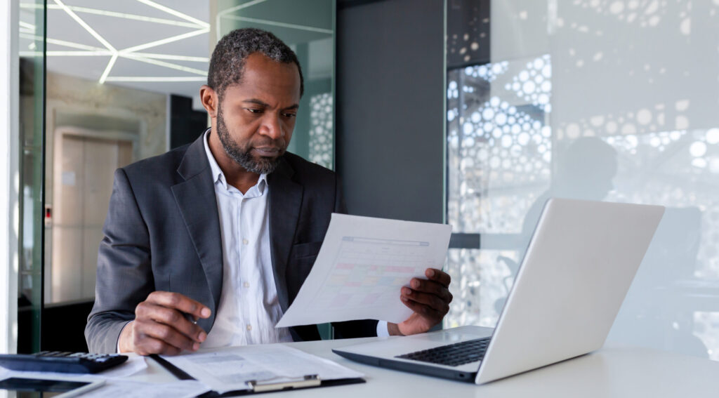 Serious senior experienced financier checking reports, african american businessman in business suit concentrating thinking working with contracts and invoices, paperwork inside office.