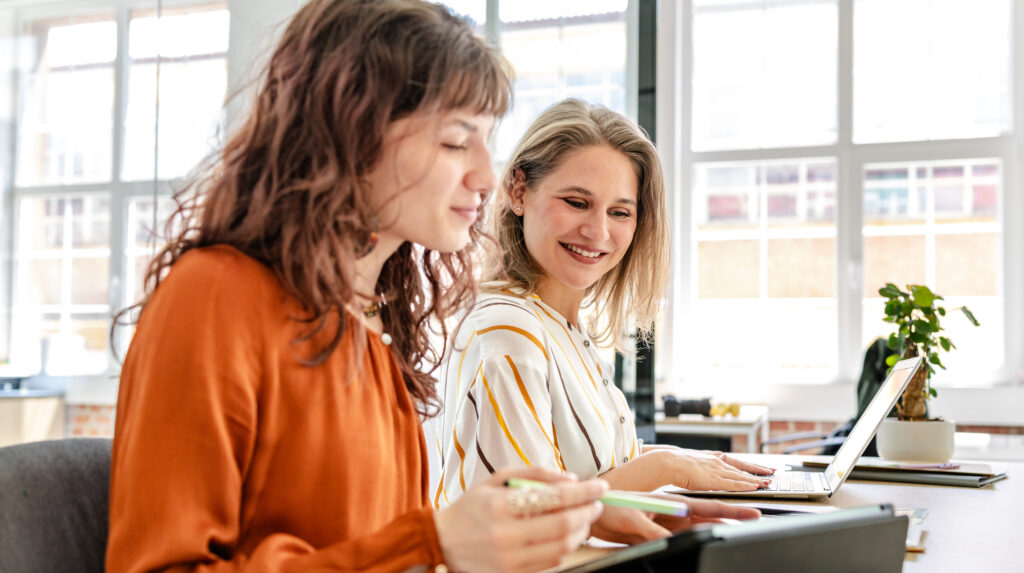 Two young businesswomen focus on their tasks in a bright modern office.